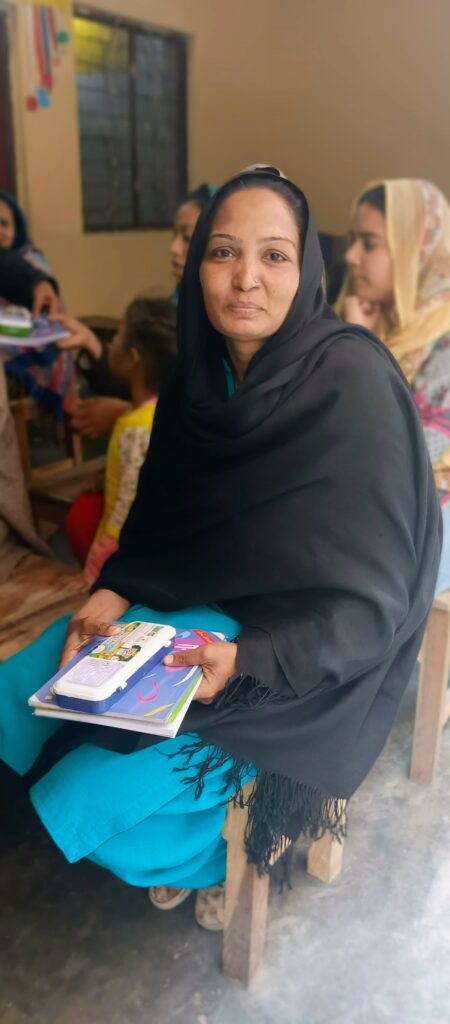 A Christian mother smiling while holding a new textbook from Chopan Trust’s Literacy Program.