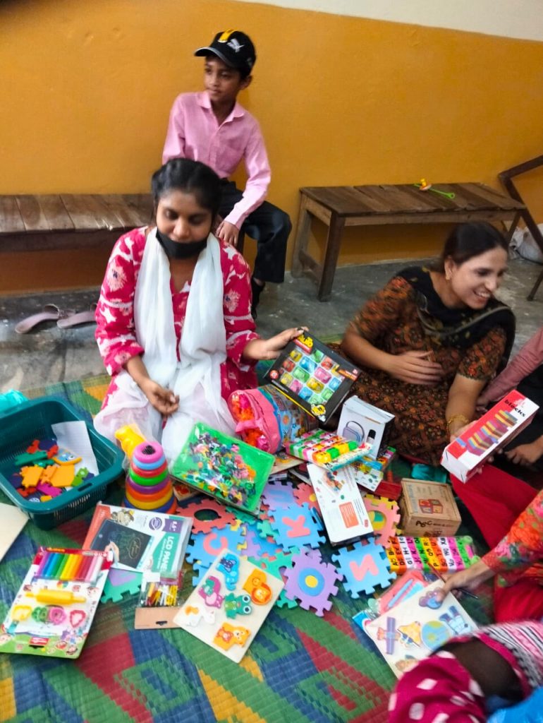 Two teachers and a boy are surrounded by a wide variety of colorful new educational toys and learning materials on a mat.